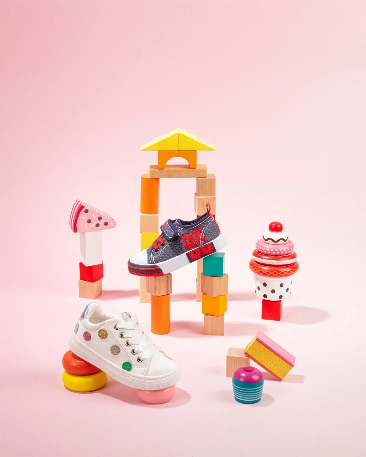 Baskets pour enfant à pois et à scratch mises en scène parmi des jeux de construction en bois, sur fond rose