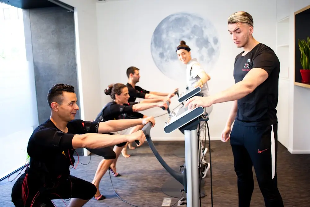 Une séance coachée dans un studio My Big Bang : des clients en tenue d’électrostimulation, guidés par un coach devant la fresque d’une lune