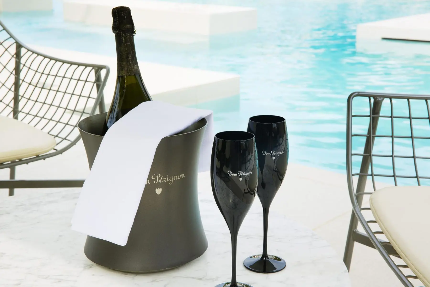 Seau à champagne et deux flûtes noires Dom Pérignon sur une table en marbre, au bord de la piscine du Sezz Saint-Tropez